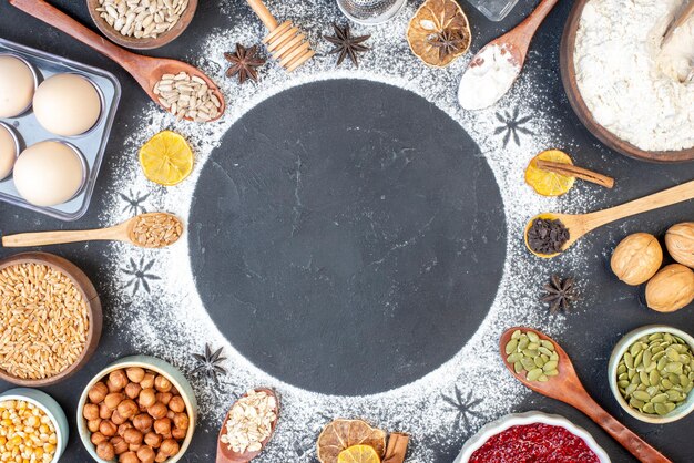 テーブルの上の木のスプーンのパン屋の材料で囲まれた小麦粉で作られた上面の円形フレーム