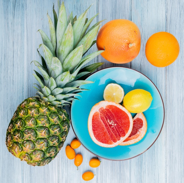 Вид сверху цитрусовых как грейпфрут и лимон в тарелке с ананасовым апельсиновым мандариновым кумкватом на деревянном фоне