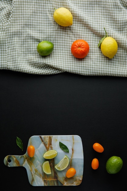 Top view of citrus fruits as lemon lime tangerine on plaid cloth with kumquats lime slices on cutting board on black background