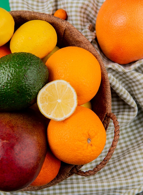 Top view of citrus fruits as mango orange avocado lemon in basket on plaid cloth background