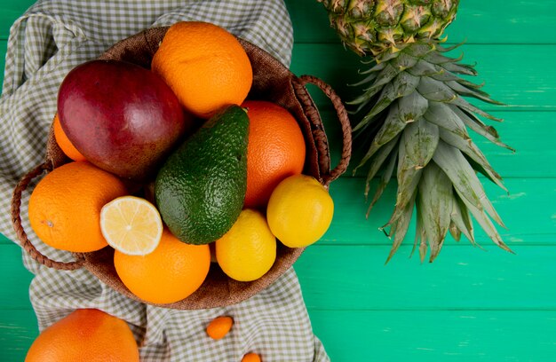 Вид сверху цитрусовых как манго оранжевый лимон авокадо в корзине с ананасом на зеленом фоне
