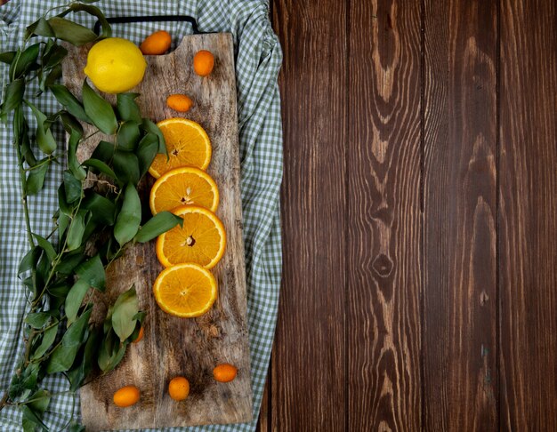 Top view of citrus fruits as orange lemon kumquat with leaves on cutting board on cloth and wooden background with copy space