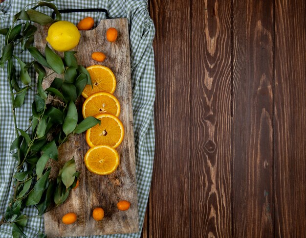 Вид сверху цитрусовых как апельсин лимон кумкват с листьями на разделочную доску на ткани и деревянный фон с копией пространства