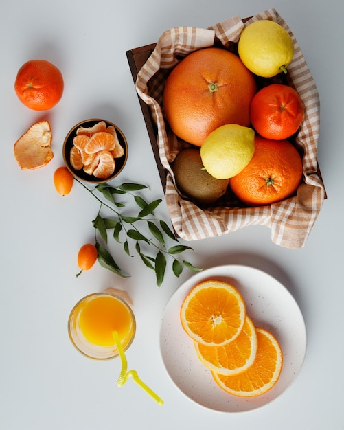 흰색 배경에 잎이 있는 오렌지 주스와 귤 껍질이 있는 접시와 그릇에 귤과 오렌지 조각이 있는 상자에 오렌지 귤 레몬 키위와 같은 감귤류 과일의 상위 뷰