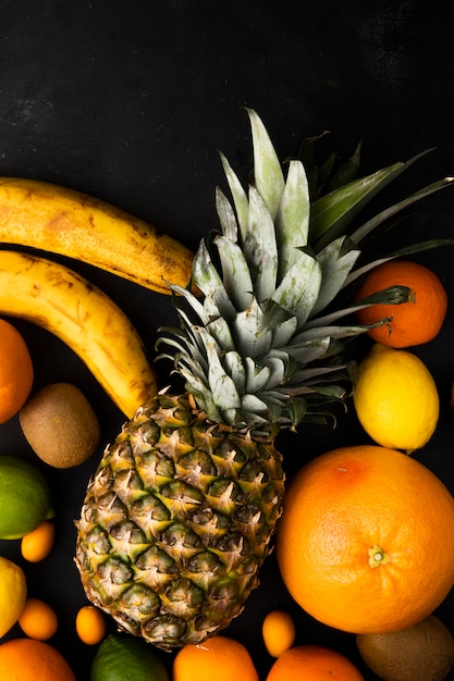 Top view of citrus fruits as pineapple orange banana and others on black surface