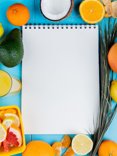 Top view of citrus fruits as tangerine avocado coconut grapefruit lemon and lemon juice with note pad on center on blue background with copy space