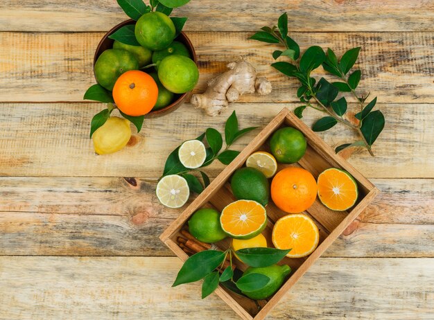 Top view of citrus fruits in a wooden bowl and crate with leaves and ginger