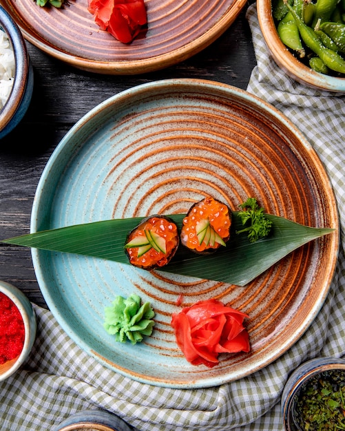 Вид сверху классических японских суши с красной икрой на листе бамбука, подается с имбирем и соусом васаби на тарелке