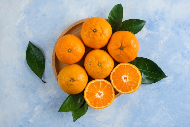 Free photo top view of clementine mandarins with leaves on wooden plate