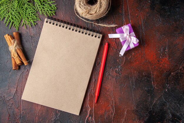 Top view of closed notebook cinnamon limes and gift on dark background