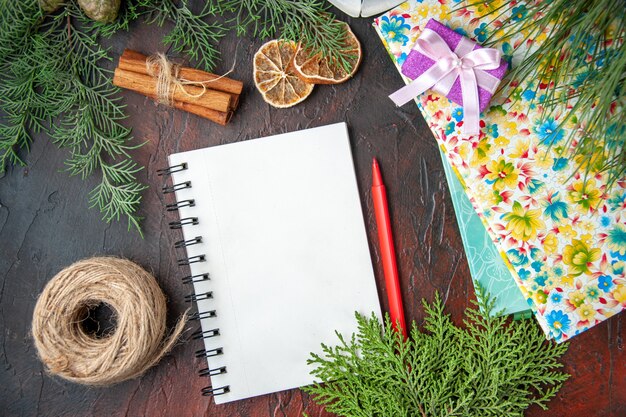 Top view of closed notebook with pen cinnamon limes a ball of rope fir branches and books on dark background