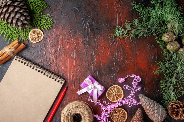 Top view of closed notebook with pen cinnamon limes and a ball of rope gift conifer cones on dark background