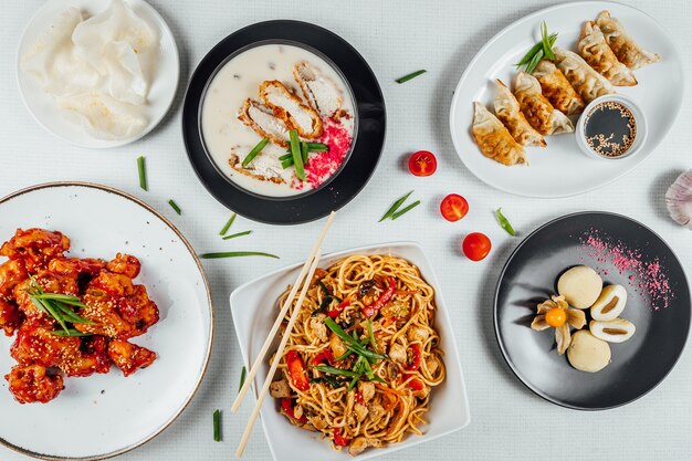 Top view closeup of the plates of Chinese foods on a white table