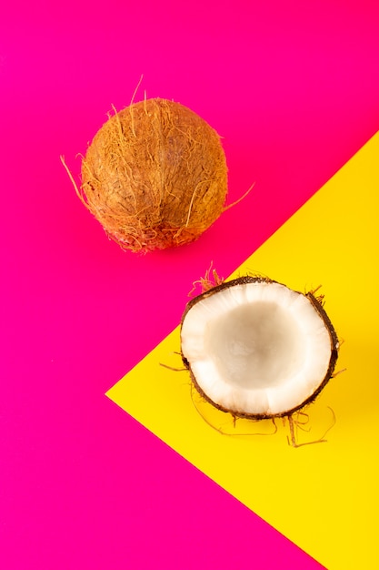 Вид сверху нарезанные кокосовые орехи и целая молочная свежая спелая, изолированные на розовый и желтый