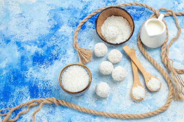 Top view coconut powder bowl coconut balls rope wooden spoons milk bowl on blue white background