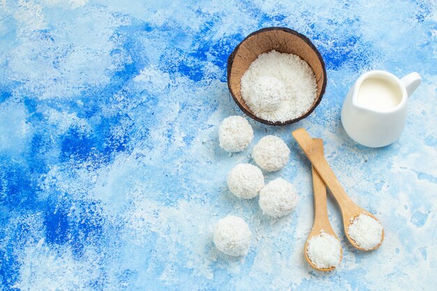 Foto gratuita vista dall'alto ciotola di polvere di cocco palle di cocco corda cucchiai di legno ciotola di latte su sfondo bianco blu