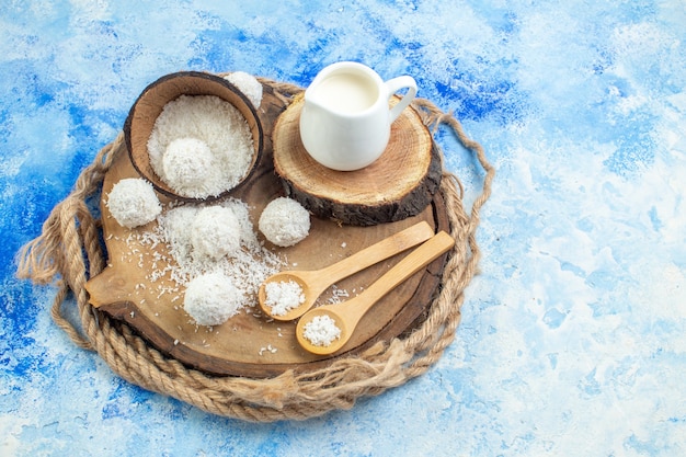 Top view coconut powder bowl coconut balls wooden spoons milk bowl on wood board rope on blue white background