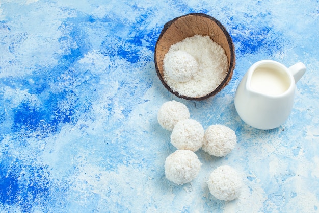 Top view coconut powder bowl milk bowl coconut balls rope wooden spoons on blue white background