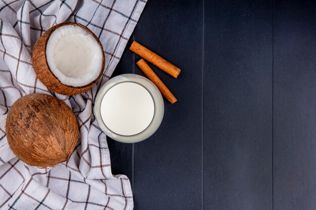 Top view of coconuts with a glass of milk with cinnamon sticks on checked tablecloth on black with copy space