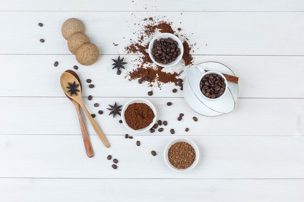 Кофейные зерна вида сверху в чашке и шаре с измельченным кофе, специями, печеньем, деревянными ложками на деревянном фоне. горизонтальный