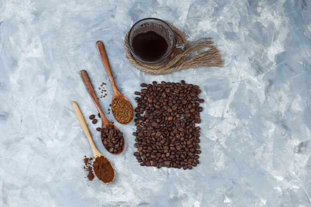 Top view coffee beans, cup of coffee with coffee beans, instant coffee, coffee flour in wooden spoons, ropes, cookies on light blue marble background. horizontal