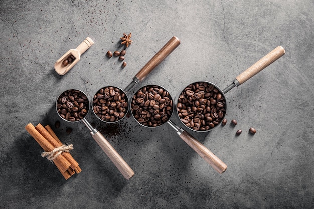 Top view of coffee beans in cups with scoop and cinnamon sticks