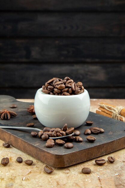 Top view of coffee beans inside and outside a small white bowl on wooden board on mixed color background