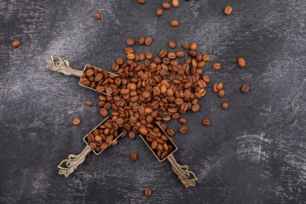 top view coffee beans in metal spoon on dark surface