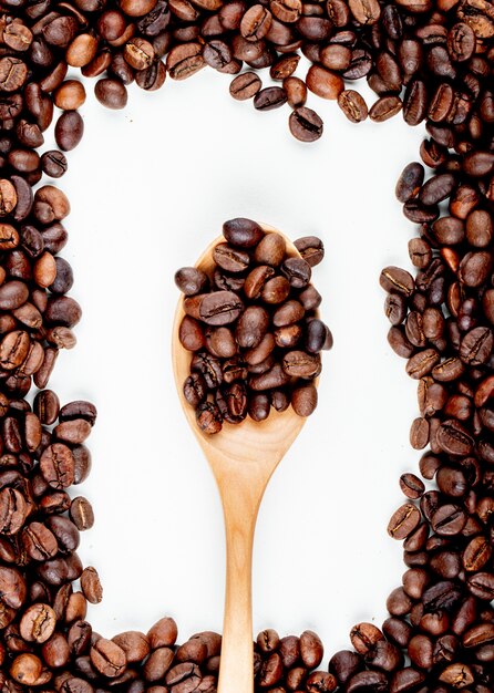 Top view of coffee beans in a wooden spoon on white background