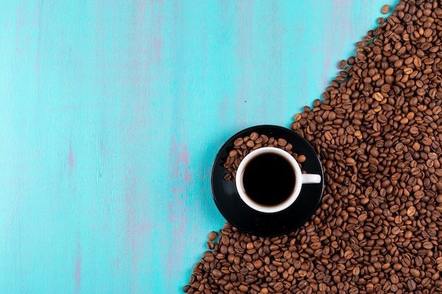 Vista dall'alto tazza di caffè con chicchi di caffè sul tavolo blu