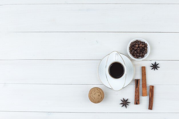 Вид сверху кофе в чашке с кофейными зернами, специями, печеньем на деревянных фоне. горизонтальный