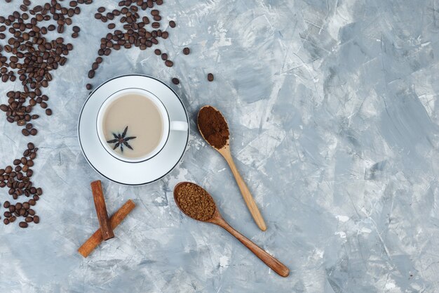 クッキー、コーヒー豆、挽いたコーヒー、灰色の石膏の背景にシナモンスティックとカップのトップビューコーヒー。水平