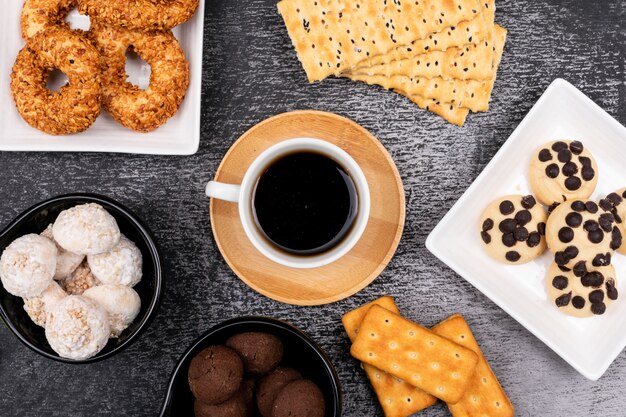 Top view coffee cup with different cookies on dark table