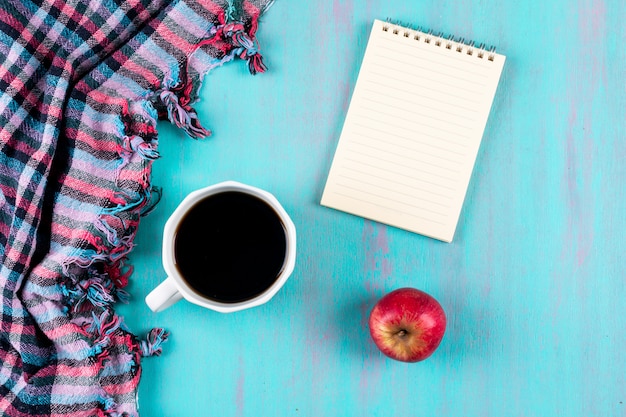 Top view coffee cup with notebook and red apple on blue table