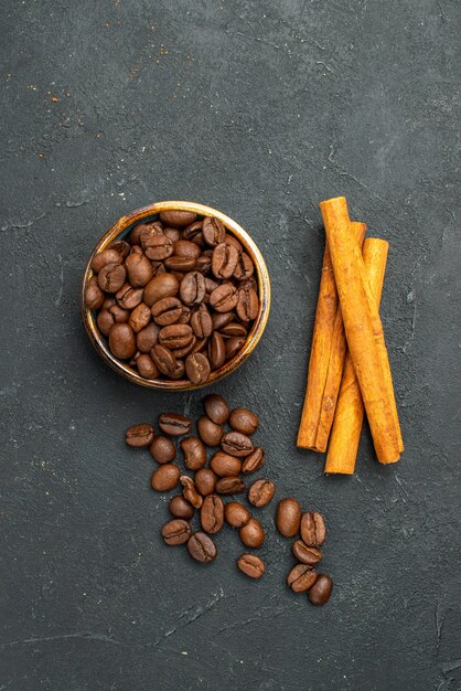 Top view coffee seeds in a bowl cinnamon sticks on dark isolated background