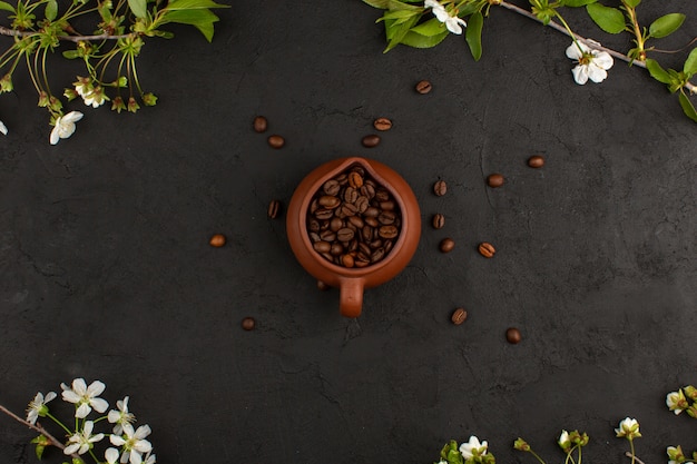 Foto gratuita vista dall'alto semi di caffè marrone intero all'interno del vaso marrone intorno a fiori bianchi sul buio