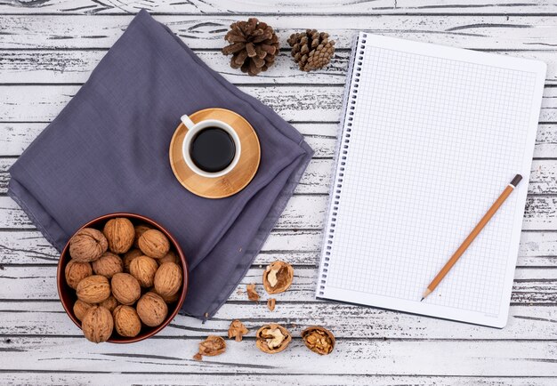 Top view of coffee with walnuts and copy space on notebook on white wooden background horizontal