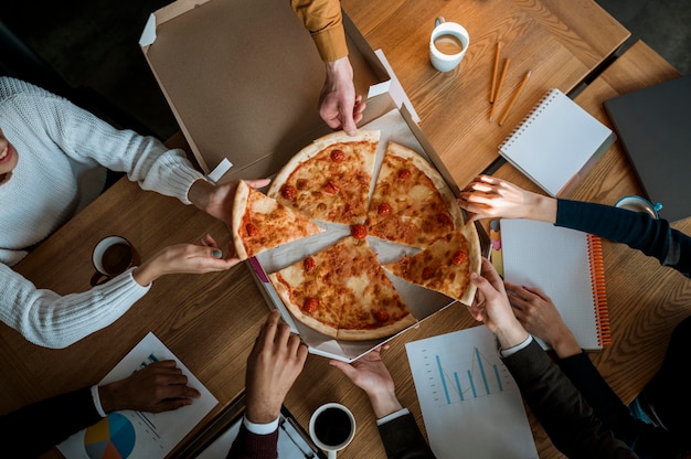 Vista dall'alto di colleghi che mangiano pizza durante una pausa di riunione in ufficio