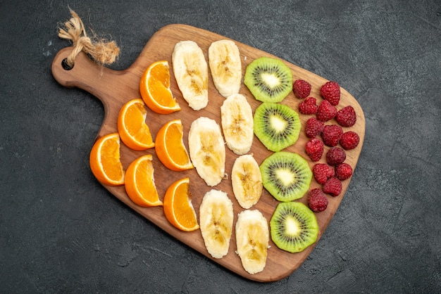 Top view of collection of chopped fresh fruits on a wooden cutting board on black table in vertical view