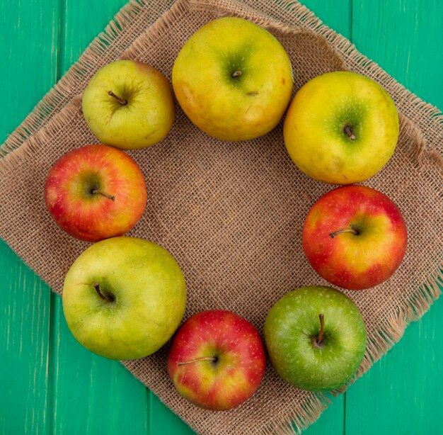 Top view of colored apples on a beige napkin on a green surface