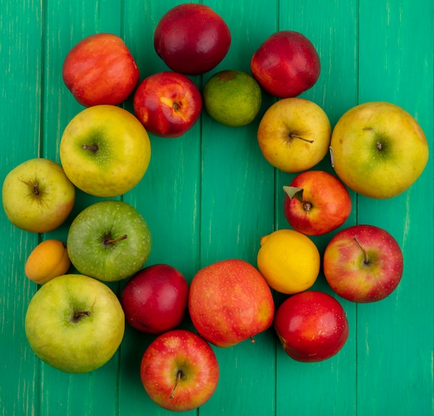Вид сверху цветных яблок с персиками, лимоном и лаймом на зеленой поверхности