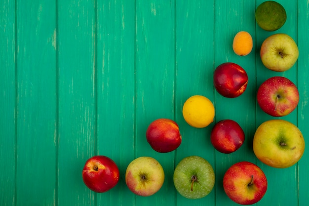 Top view of colored apples with peaches and lemon with lime on a green surface