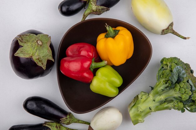 Top view colored bell pepper in a bowl with eggplant and broccoli on a white background