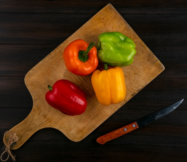 Top view of colored bell peppers on a cutting board with a knife on a wooden surface