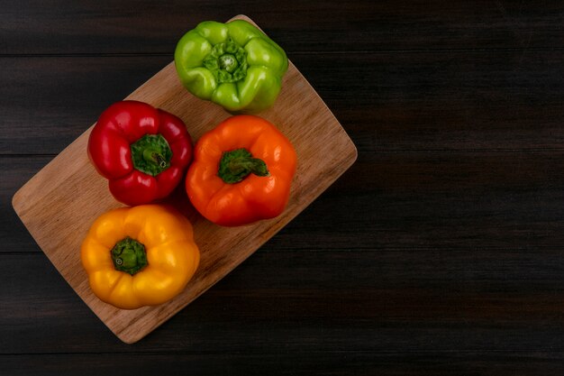 Top view of colored bell peppers on a cutting board on a wooden surface