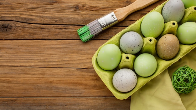 Free photo top view of colored easter eggs in carton with paint brush and copy space