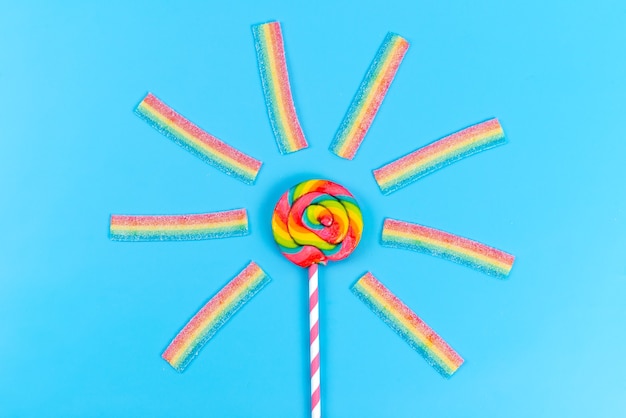 A top view colored lollipop along with chewing marmalades on blue