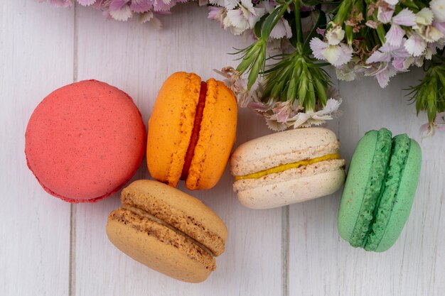 Top view of colored macarons with flowers on a white surface