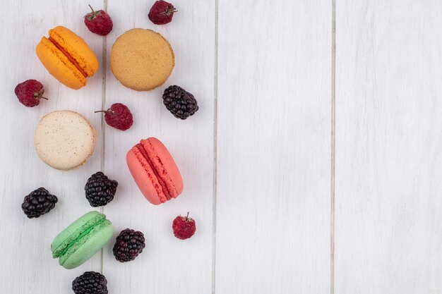 Top view of colored macarons with raspberries and blackberries on a white surface