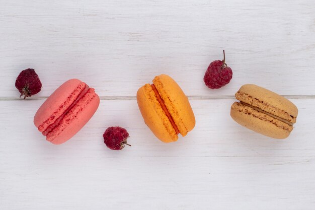 Top view of colored macarons with raspberries on a white surface